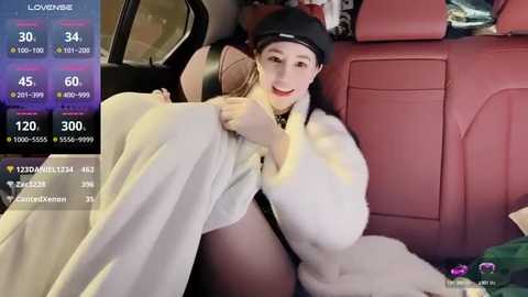 Media: Video of a young woman with fair skin, light brown hair, and a black beanie, lounging in a car seat, wrapped in a white fur coat. Background shows a pink leather interior.