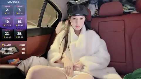 Media: Video of a young woman with fair skin, long black hair, wearing a black headband and white fur coat, sitting in a car, partially nude, revealing her vagina, with digital information overlay.