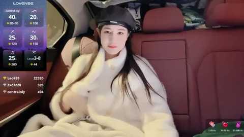 Media: Video of a young East Asian woman with long black hair, wearing a black beanie and white fur coat, lying in a car seat.