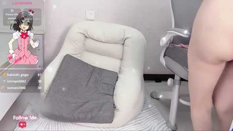 Media: Video of a woman in a grey dress reclining on a white couch, with a black cushion beside her. A poster of an anime character is on the left wall.