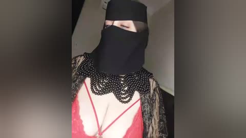 Media: Video of a woman in a black hijab and red lace bra, with a black beaded necklace, wearing a black headscarf.