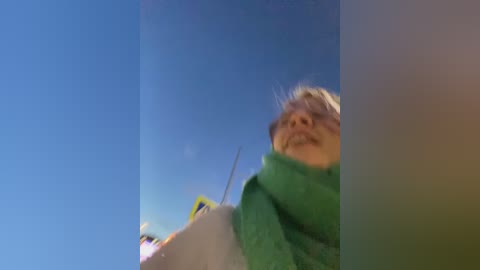 Media: Video of a smiling elderly person with light skin, wearing a green sweater, looking up at a clear blue sky.