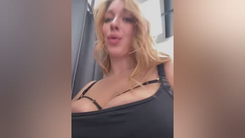 Media: Video of a blonde woman with large breasts, wearing a black bra, standing in a bathroom. The image is blurry, with a focus on her chest.