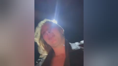 Media: Video of a blonde woman in a black jacket, her hair blowing, with a bright light shining from the left, creating a dramatic effect.