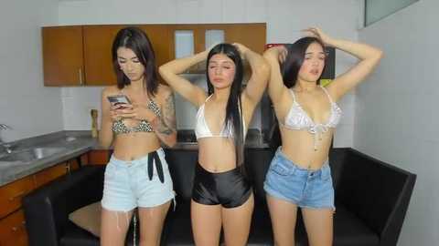 Media: Video of three young women in revealing bikinis, one in leopard print, one in white, one in black, posing in a modern kitchen.