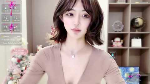 Media: A video of a young East Asian woman with straight, shoulder-length dark hair, wearing a V-neck top, in a modern living room with a Christmas tree and bookshelves in the background.