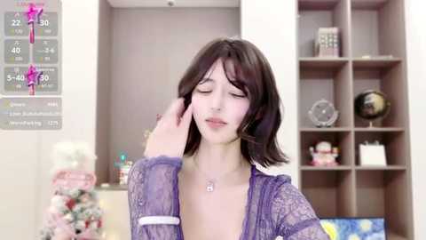 Media: A video of a young woman with fair skin and shoulder-length brown hair, wearing a purple lace robe, touching her hair, in a modern living room with shelves and a globe.