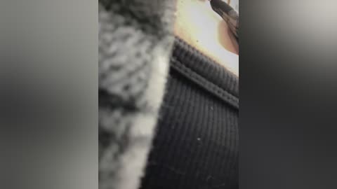 Media: A close-up video of a person's hand holding a black, textured sweater with white, textured fabric on the left side. The background is blurred and out of focus, emphasizing the textures and contrast between the two materials.