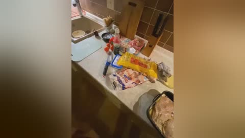 Media: Video of a messy kitchen countertop with a partially mixed bowl of brown batter, various open packages, and utensils, set against beige tiled walls.