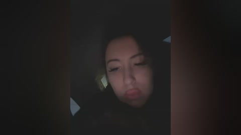 Media: Video of a young Asian woman with straight black hair, wearing a dark jacket, looking tired and slightly pouty, her eyes closed, in a dimly lit room.