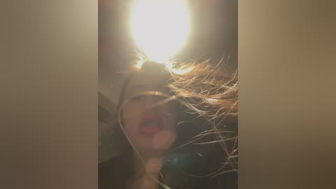 Media: Video of a woman with long, light brown hair, wearing red lipstick, captured from above with a bright light source creating a halo effect around her head.