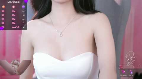 Video of a light-skinned woman with long black hair, wearing a white strapless dress and a delicate necklace, against a pink and white backdrop.