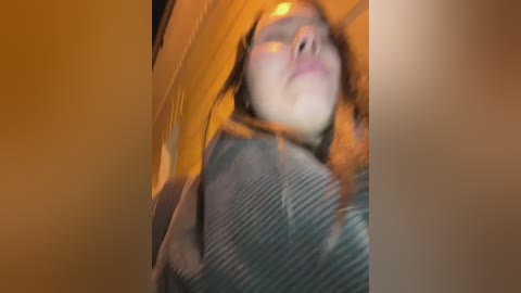 Media: A blurred, close-up video of a woman with reddish-brown hair wearing a striped shirt, possibly in a car, with warm, yellowish-orange light casting a soft glow.