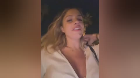 Media: Video of a smiling woman with wavy blonde hair, wearing a white robe, leaning back with one hand on her neck.