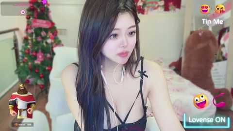 Media: Video of a young Asian woman with long black hair, wearing a black lace bra, sitting on a bed decorated with Christmas ornaments. Background shows a festive room.