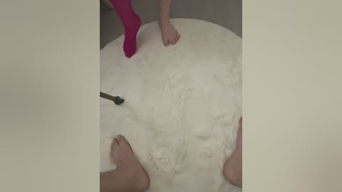 Media: A video shows two legs and a pink sock on a large, fluffy white mat, possibly in a bathroom, with a black drain cover in the background.