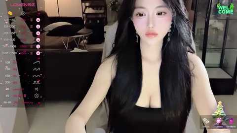 Media: A video of an East Asian woman with long black hair, wearing a black sleeveless top, sitting indoors. The background shows a modern living room with a black sofa and glass doors.