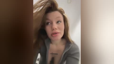 Media: Video of a light-skinned woman with brown hair, wearing a gray hoodie, looking surprised, partially obscured by a brown object.