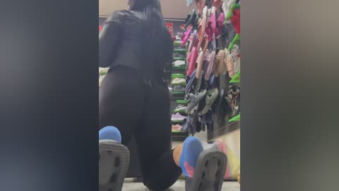 Media: Video of a person wearing black clothing and blue sneakers, standing in a brightly lit shoe store filled with colorful shoes on shelves.