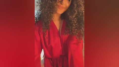 Media: Video of a woman with curly, voluminous hair wearing a red robe, partially cropped from the shoulders down. The background is a gradient of reds.