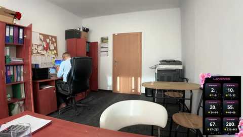 Media: Video of a modern office with a white desk, a man in a blue shirt working on a computer, wooden bookshelves, and a London weather forecast screen.