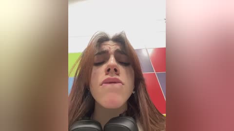 Media: Video of a woman with long brown hair, wearing black headphones, closing her eyes in a tiled bathroom with vibrant colors.