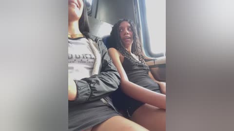 Media: Video of two women, one with long curly hair in a black dress, the other in a white t-shirt, sitting in a bus.