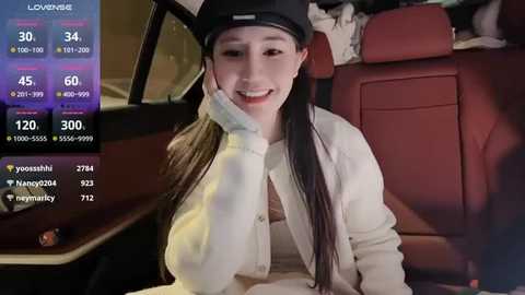 Media: A video of an East Asian woman with long black hair and fair skin, smiling in a car, wearing a white coat and black hat, with a digital screen showing live stream metrics.