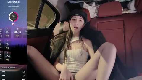 Media: Video of a young Asian woman with long, straight hair, wearing a black beanie and beige tank top, sitting provocatively in a car, with a blurred cityscape and navigation screen visible.