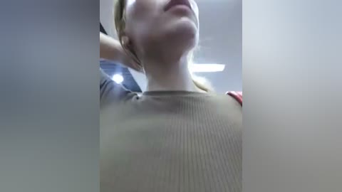 Media: Video of a woman with light skin and blonde hair, wearing a ribbed, beige tank top, captured from a low angle, with blurred background.