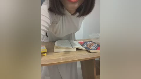 Video of a woman with straight, dark hair, wearing a white lab coat, bent over a wooden table, reading a book titled \"The Art of War.\