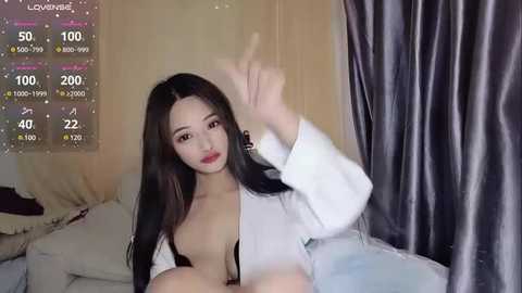 Media: A video of an Asian woman with long black hair, fair skin, and a slender physique, wearing a revealing white shirt, lying on a bed with beige and grey curtains in the background.