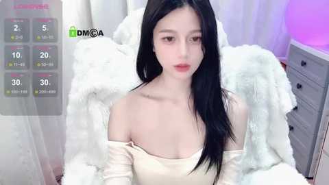 Media: A video of an East Asian woman with long black hair, fair skin, and a petite figure, wearing a white off-shoulder top, sitting on a bed with white fur blankets. The room has white curtains and a gray dresser.