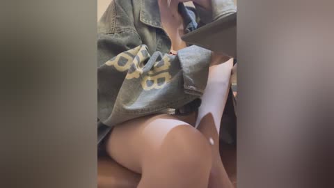 Media: Video of a person with light skin tone, wearing a loose, grey T-shirt, and partially visible white underwear, sitting on a wooden floor.