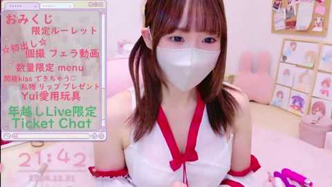 Media: Video of an Asian woman with light skin and straight brown hair, wearing a white mask, sleeveless red dress, and red arm sleeves, in a bright, pink-themed room. Text in Japanese and English overlays the image.