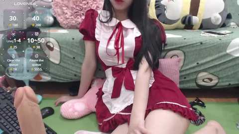 Media: Video of an East Asian woman in a red maid outfit, sitting on a green floor with plush toys and scattered items, with a virtual reality interface overlay.