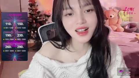 Media: Video of an Asian woman with long black hair, wearing a white off-shoulder sweater, smiling. Background features a Christmas tree, teddy bear, and \"Patreon\" logo.