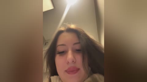 Media: A video of a young woman with fair skin and long brown hair, wearing light makeup, captured from a low angle, looking upward. The background is dimly lit, suggesting an indoor setting.