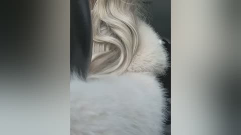 Media: A video of a person with wavy, platinum blonde hair and a white fur coat, seen from the back, with blurred out faces.