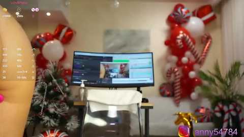 Media: Video of a modern, festive living room featuring a white, curved computer monitor displaying a social media feed, red and white candy cane decorations, a white Christmas tree, and a gold gift box in the foreground.