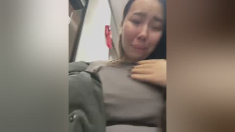 Media: Video of an Asian woman with dark hair, wearing a gray sweater, lying on a train seat with her head on a man's shoulder. Background shows train interior with blurred objects.