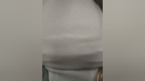 Media: A close-up video of a woman's torso in a white, ribbed knit top, with blurred background. The top has a snug fit, emphasizing her medium-sized breasts and slender waist.