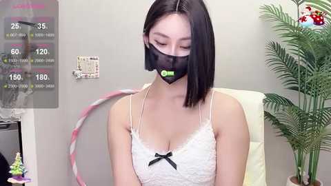 Media: Video of an Asian woman with straight black hair, wearing a white lace bra, black face mask, and green headphones, seated in a modern office setting with a potted plant and wall calendar.