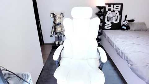 A video of a modern bedroom with a white ergonomic chair, gray bed, black wall art, and a robotic bear.