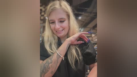 Media: A video of a blonde woman with long hair, wearing a black shirt, smiling and playing with her hair in a salon setting.