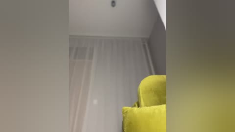 Media: Video of a minimalist room with a bright yellow armchair, soft white curtains, and a small, round ceiling light. The room has a modern, clean aesthetic with neutral wall colors.