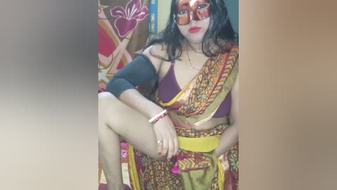 Media: Video of a plus-size South Asian woman with dark hair, wearing a colorful sari, a red mask, and a black sleeve, sitting on a bed.