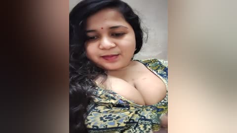 Media: A video of a South Asian woman with long, wavy black hair, fair skin, and a red dot on her forehead. She is wearing a low-cut, colorful floral dress, showing cleavage.