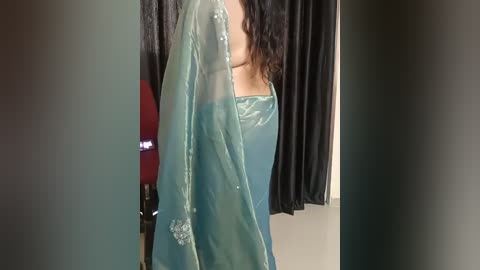 Media: Video of a person wearing a green, see-through chiffon dupatta draped over a dark outfit, partially revealing their chest. Background features a black curtain and a red lamp.