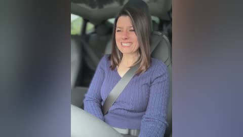 Media: A video of a smiling woman with straight, shoulder-length brown hair, wearing a purple knit sweater, seated in a car with a seatbelt across her chest. The car's interior is visible in the background.